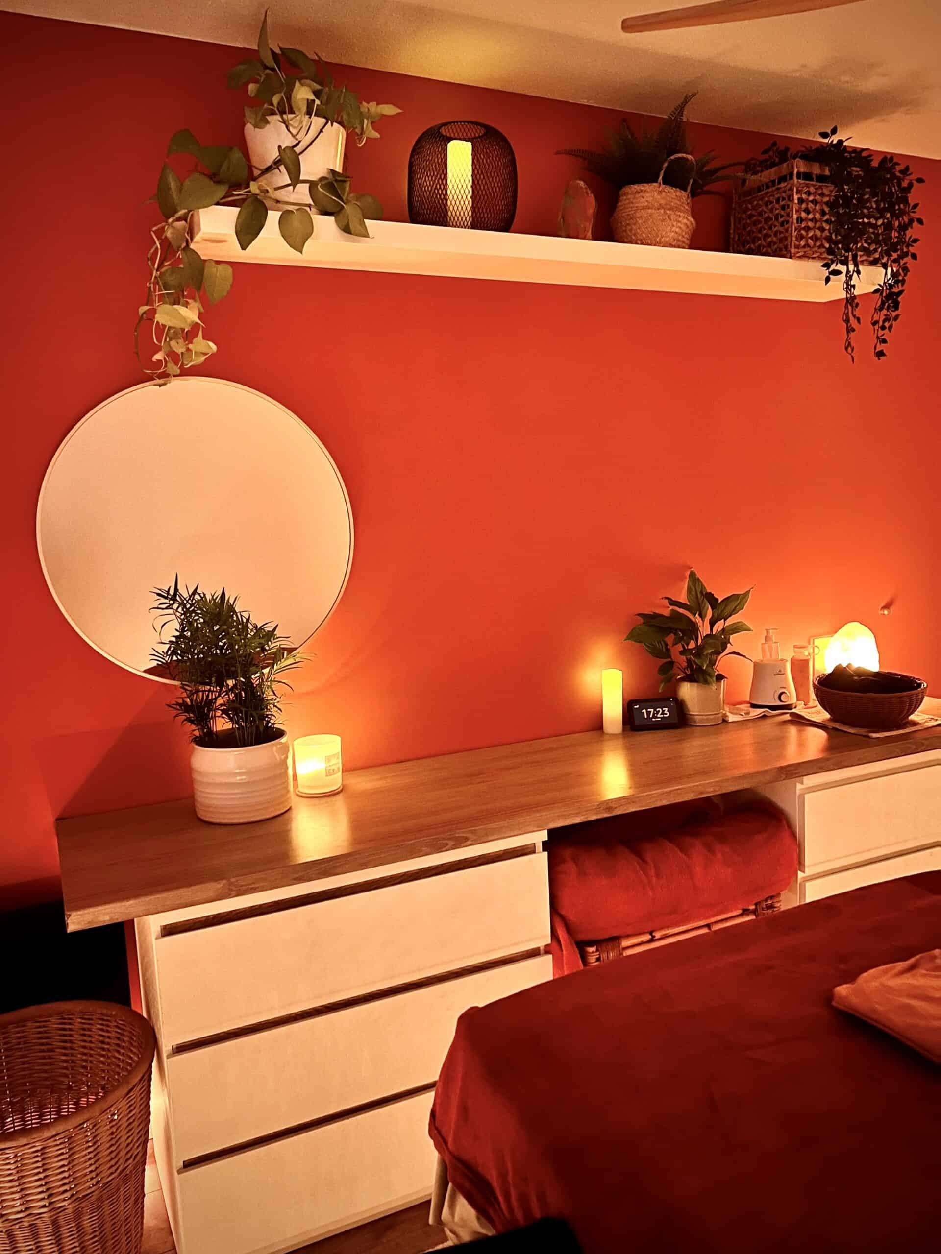 Mur rouge, miroir, plantes et espace de préparation dans le salon de massage de Laure
